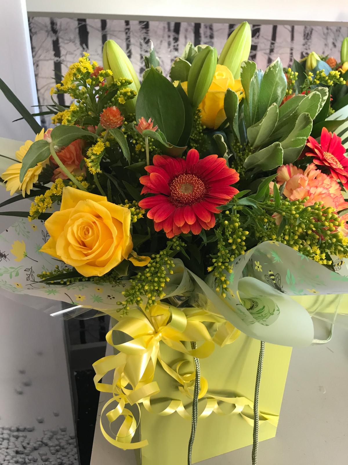 A Gift Bag Bouquet containing yellow and orange brightly coloured flowers