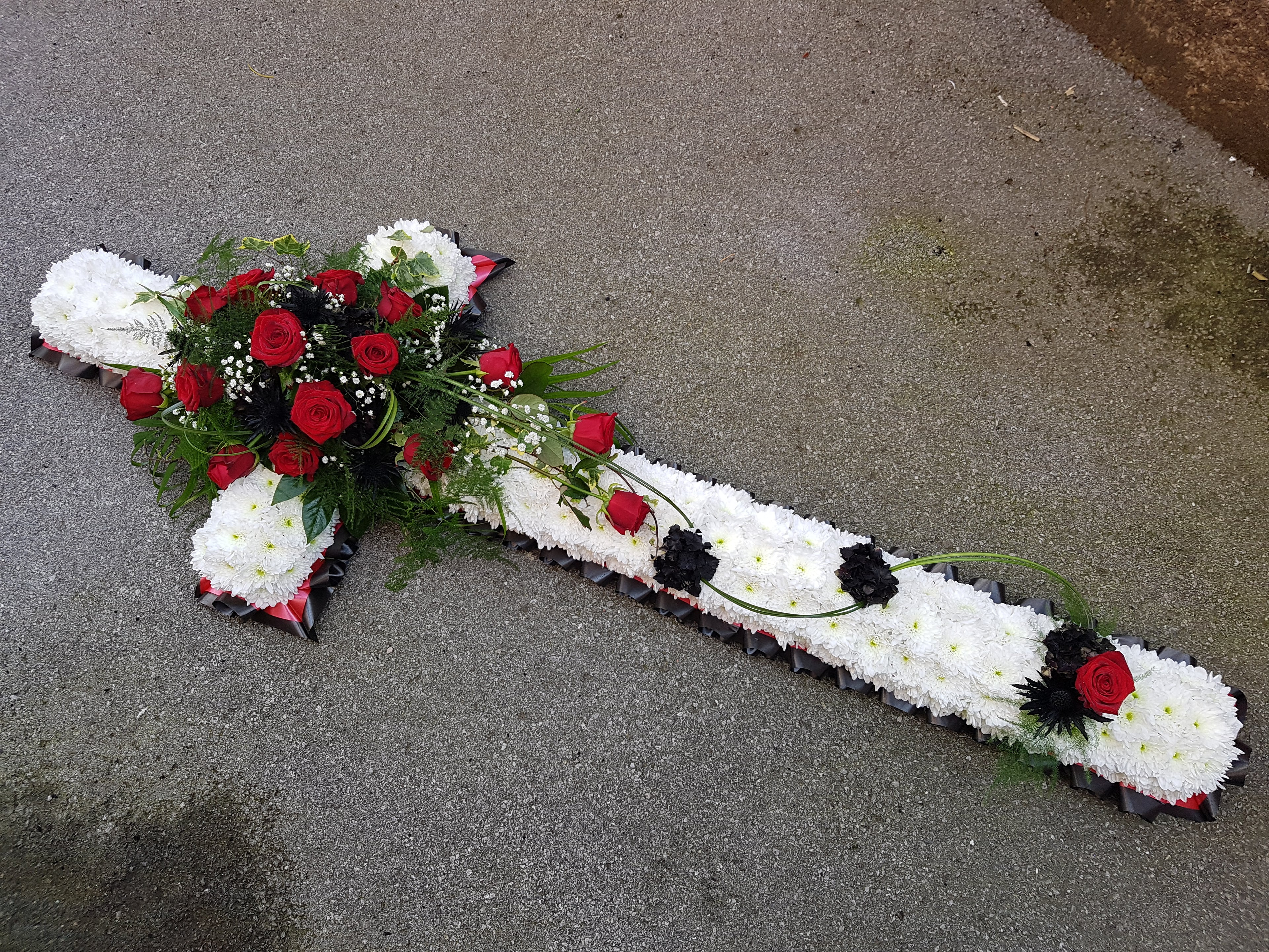 white floral cross with red ribbon and sprays